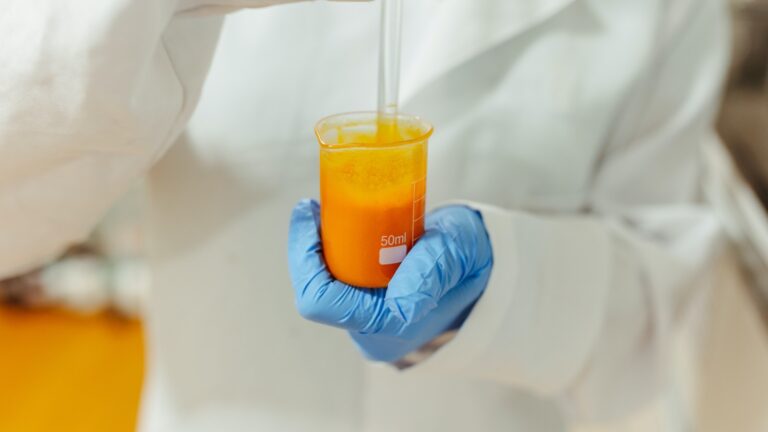Closeup of a Scientist Wearing a Lab Coat and Blue Gloves Testing a Yellow Liquid